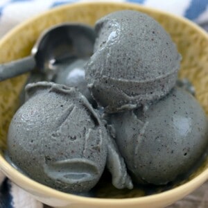 a bowl with blueberry ice cream and a spoon along side a blue and white striped napkin.