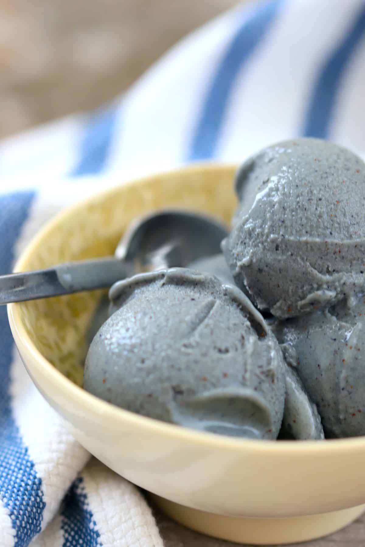 a bowl with blueberry ice cream and a spoon along side a blue and white striped napkin.