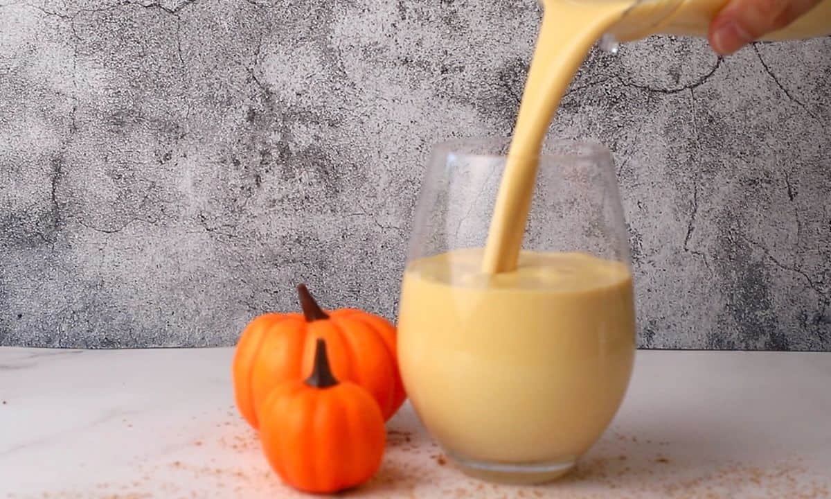 pouring the pumpkin smoothie into a glass next to a mini pumpkin ornament.