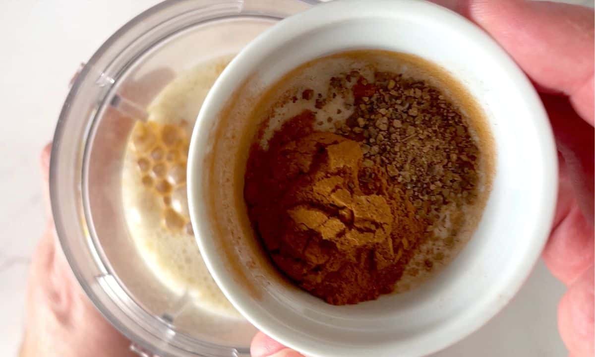 small white bowl with spices above the blender cup.