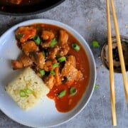a dish with keto bourbon chicken and a side of cauliflower rice topped with green onions and sesame seeds.