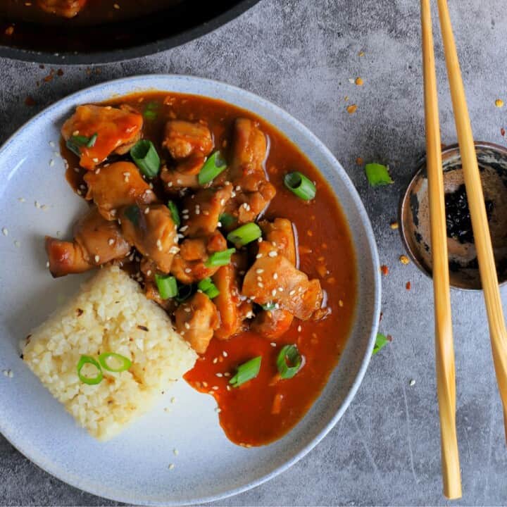 a dish with keto bourbon chicken and a side of cauliflower rice topped with green onions and sesame seeds.