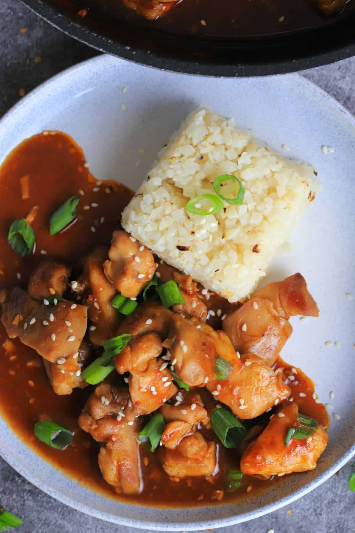 keto bourbon chicken with a side of rice topped with sesame seeds and green onions.