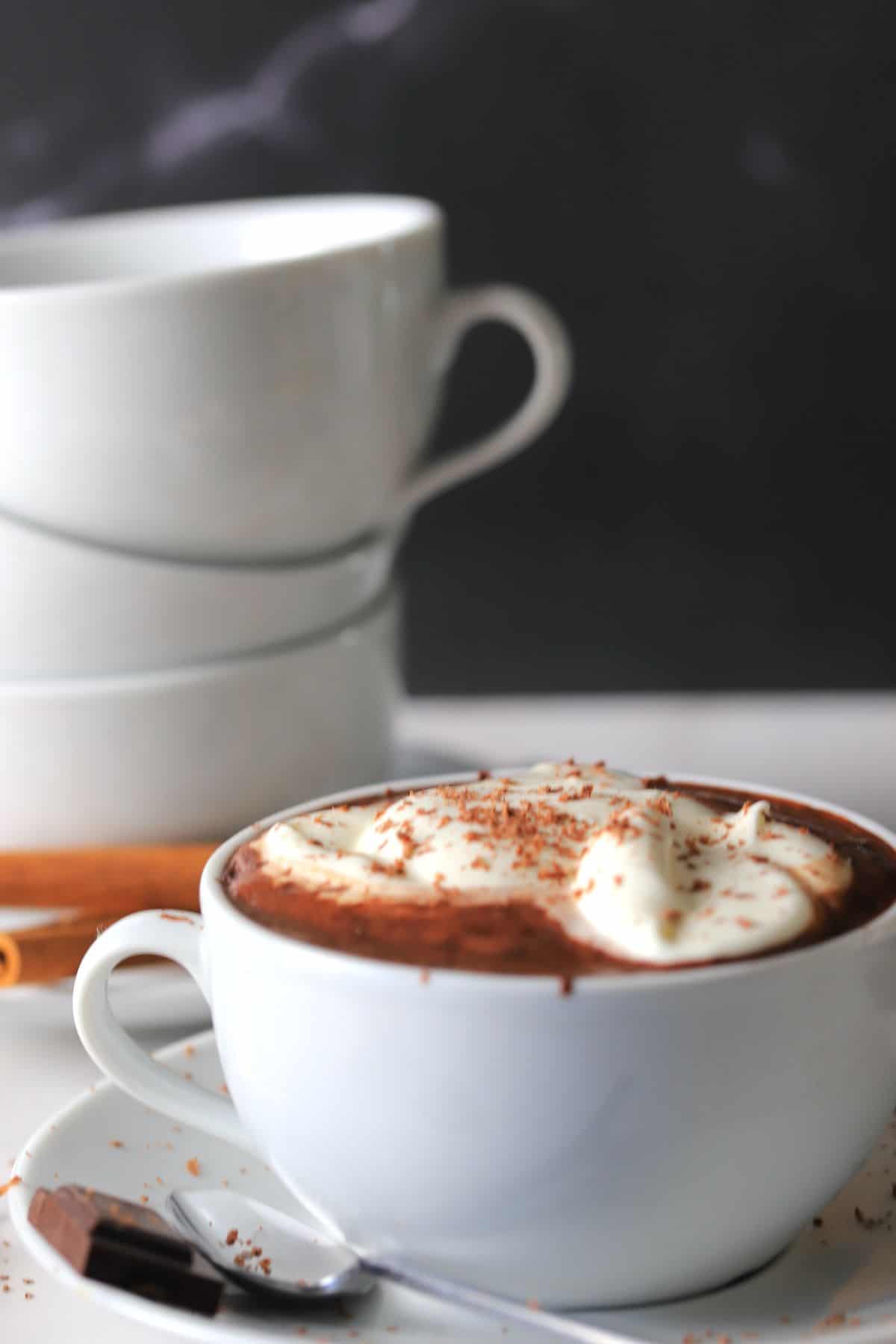 white cup full of hot chocolate with 3 white cups stacked on the side.