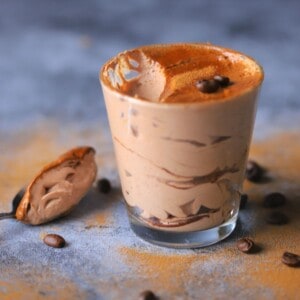 keto tiramisu mousse in a tumbler with a spoon resting on it's side with coffee beans.