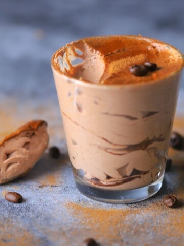 keto tiramisu mousse in a tumbler with a spoon resting on it's side with coffee beans.