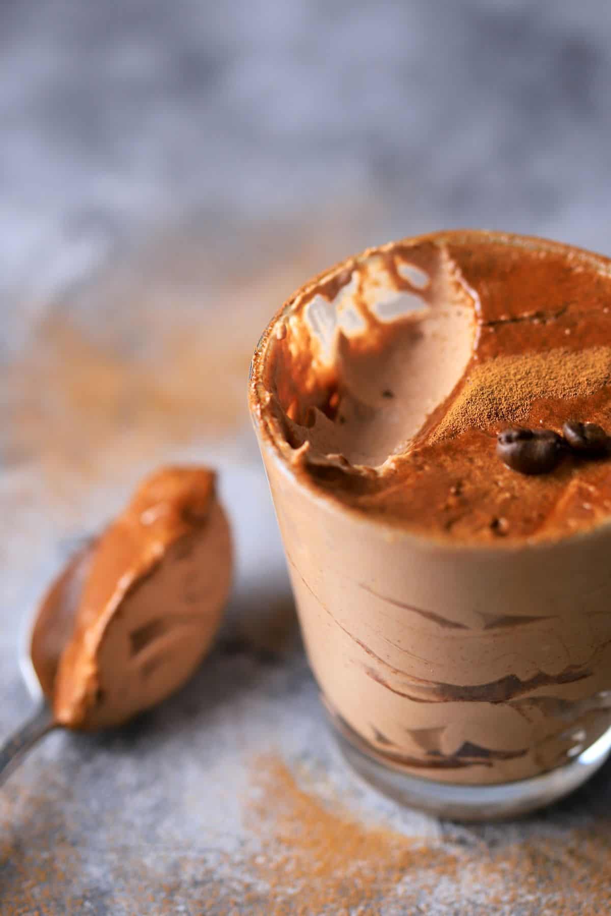 keto tiramisu mousse in a tumbler with a spoon resting on it's side with coffee beans.