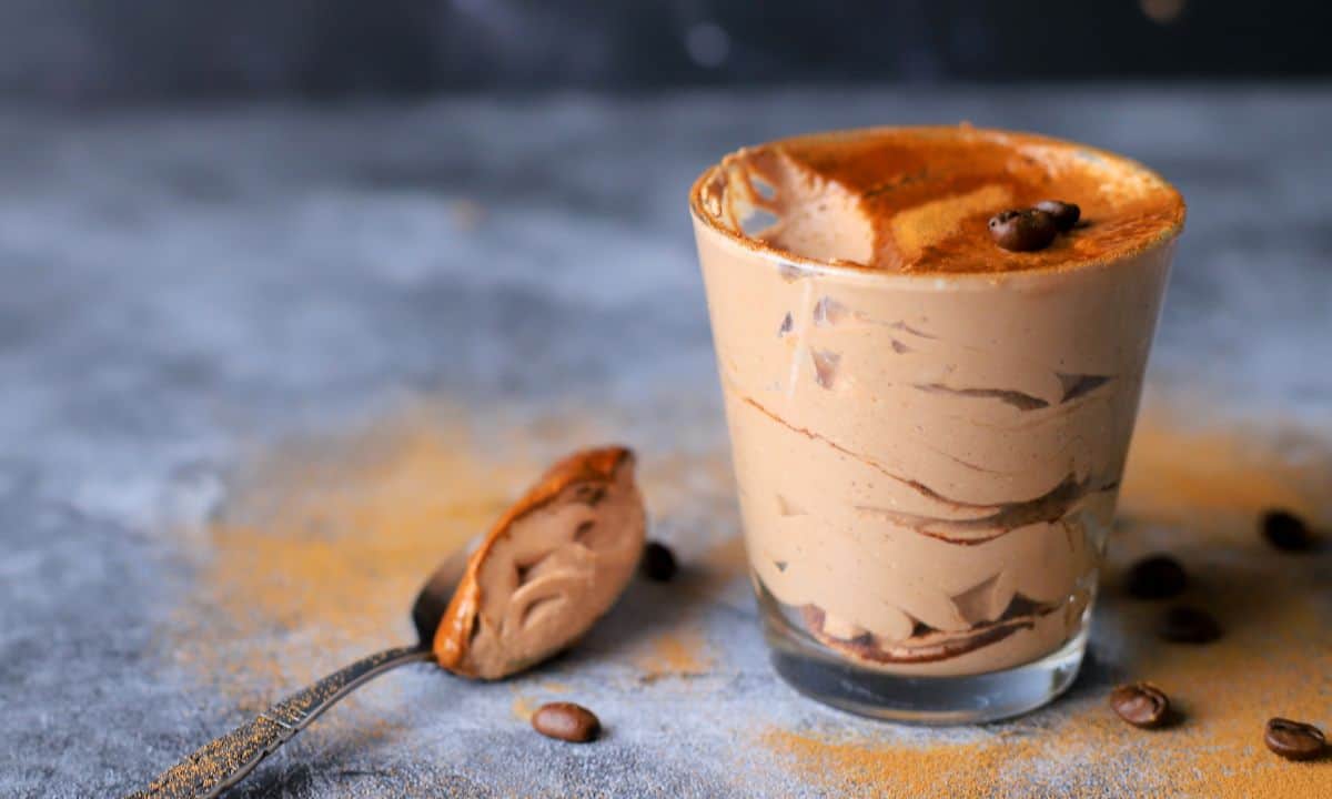 keto tiramisu mousse in a tumbler with a spoon resting on it's side with coffee beans.