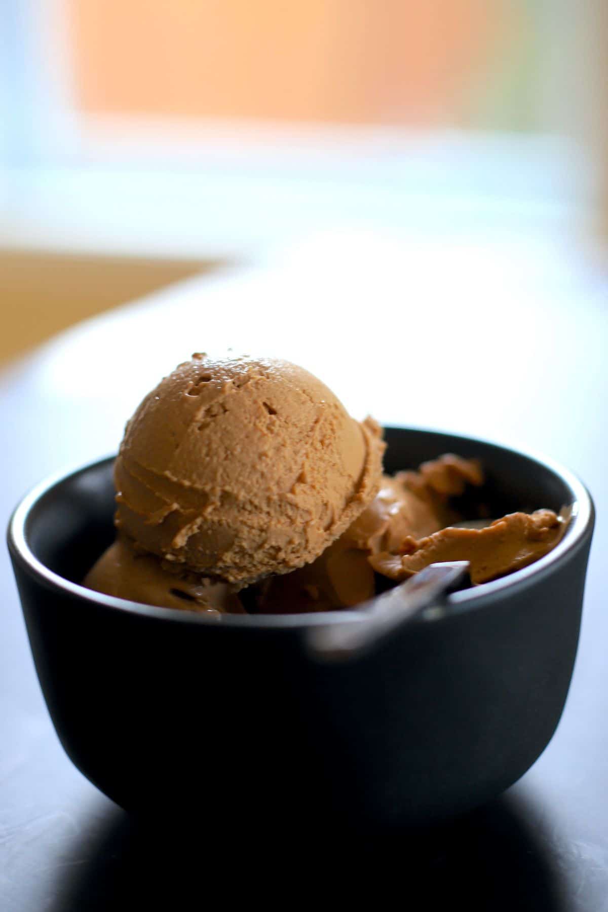 black bowl with tiramisu ice cream and a silver spoon next to a window.