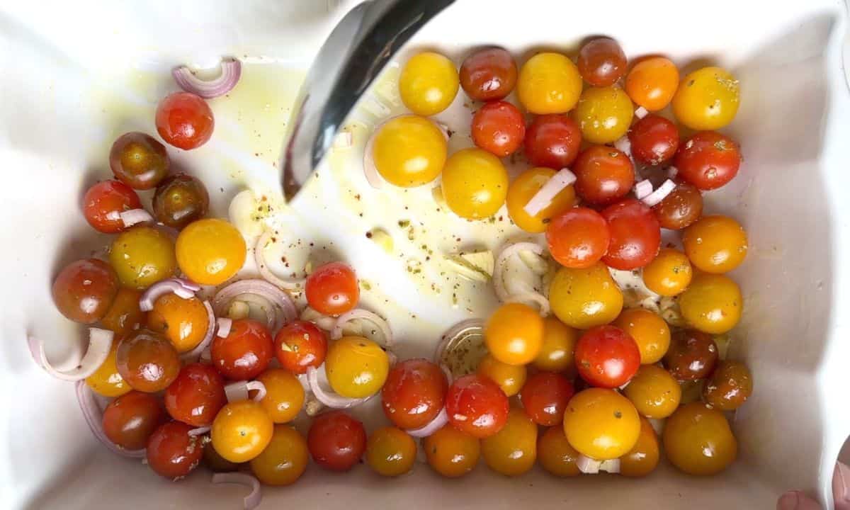 a spoon mixing fresh tomatoes in a casserole dish with sliced garlic and shallots.