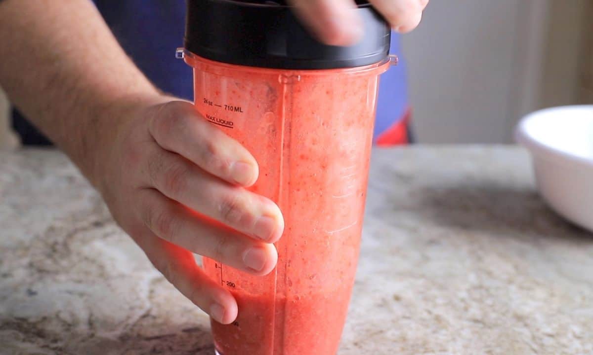 twisting blender cap blades onto blender cup full of strawberry mixture.