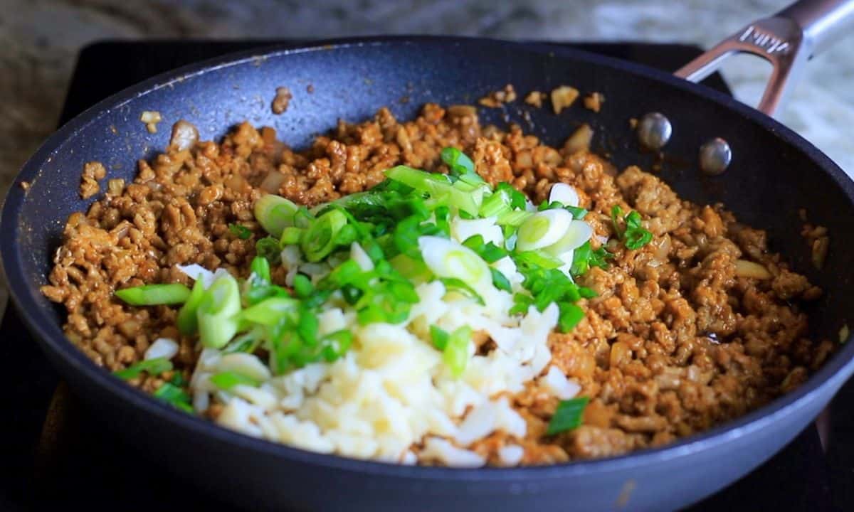 frying pan with ground chicken topped with green onions and diced water chestnuts.