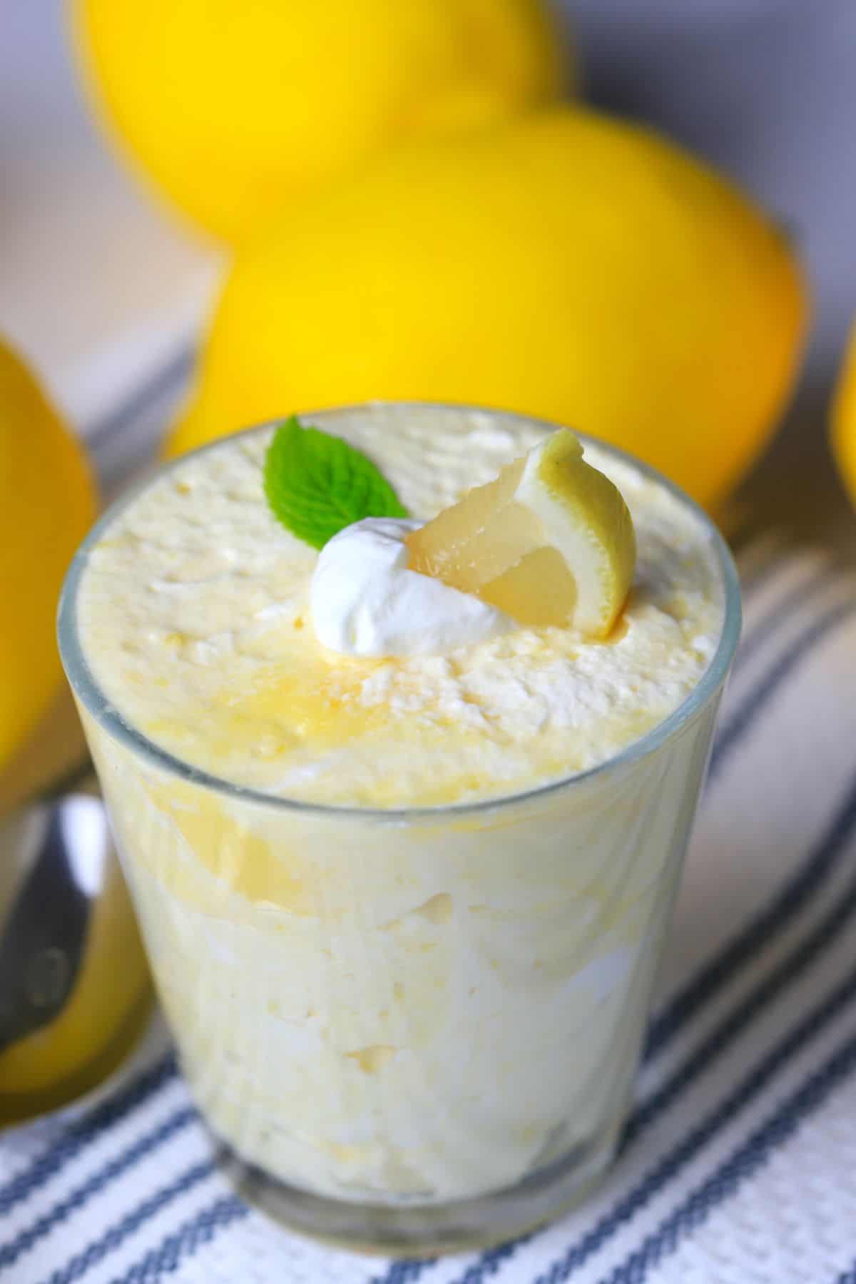 lemon mousse in a glass cup topped with a dollop of whip cream, a lemon wedge and a mint leaf.