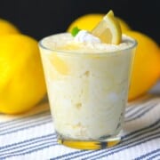 lemon mousse in a glass cup topped with a dollop of whip cream, a lemon wedge and a mint leaf.