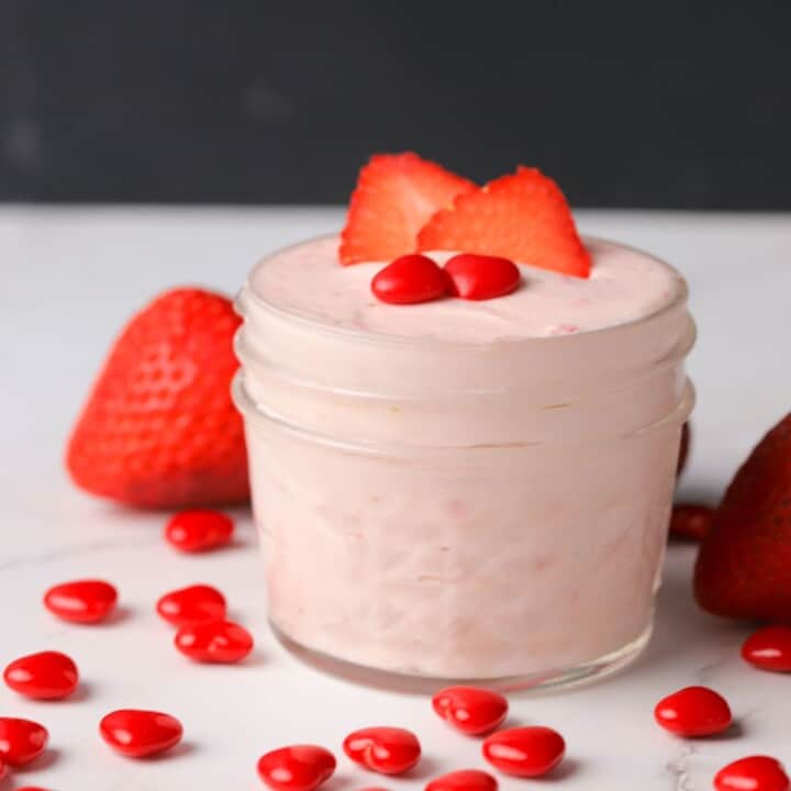 keto strawberry mousse in a small glass jar topped with strawberry slices and two cinnamon hearts.