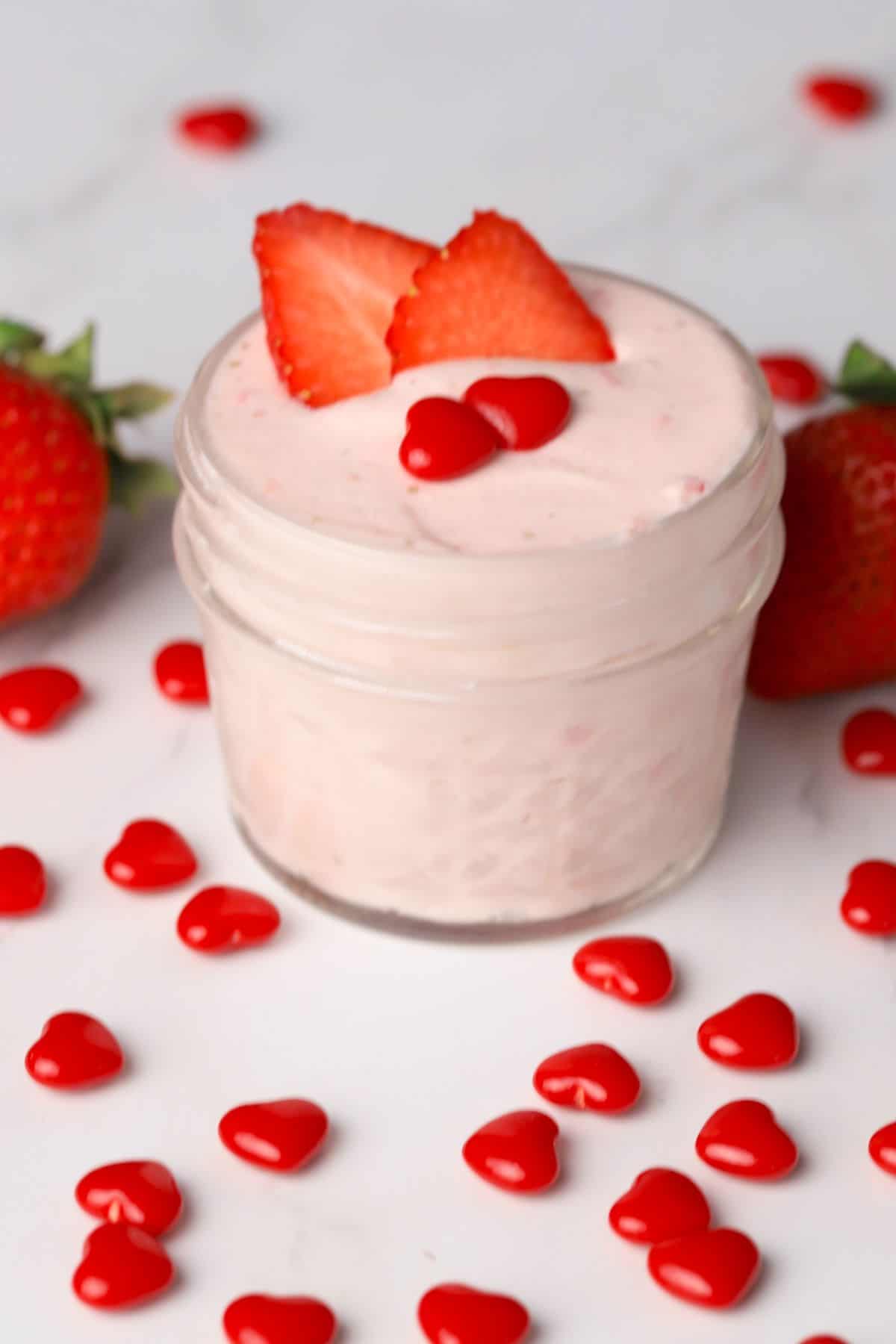 keto strawberry mousse in a small glass jar topped with strawberry slices and two cinnamon hearts.