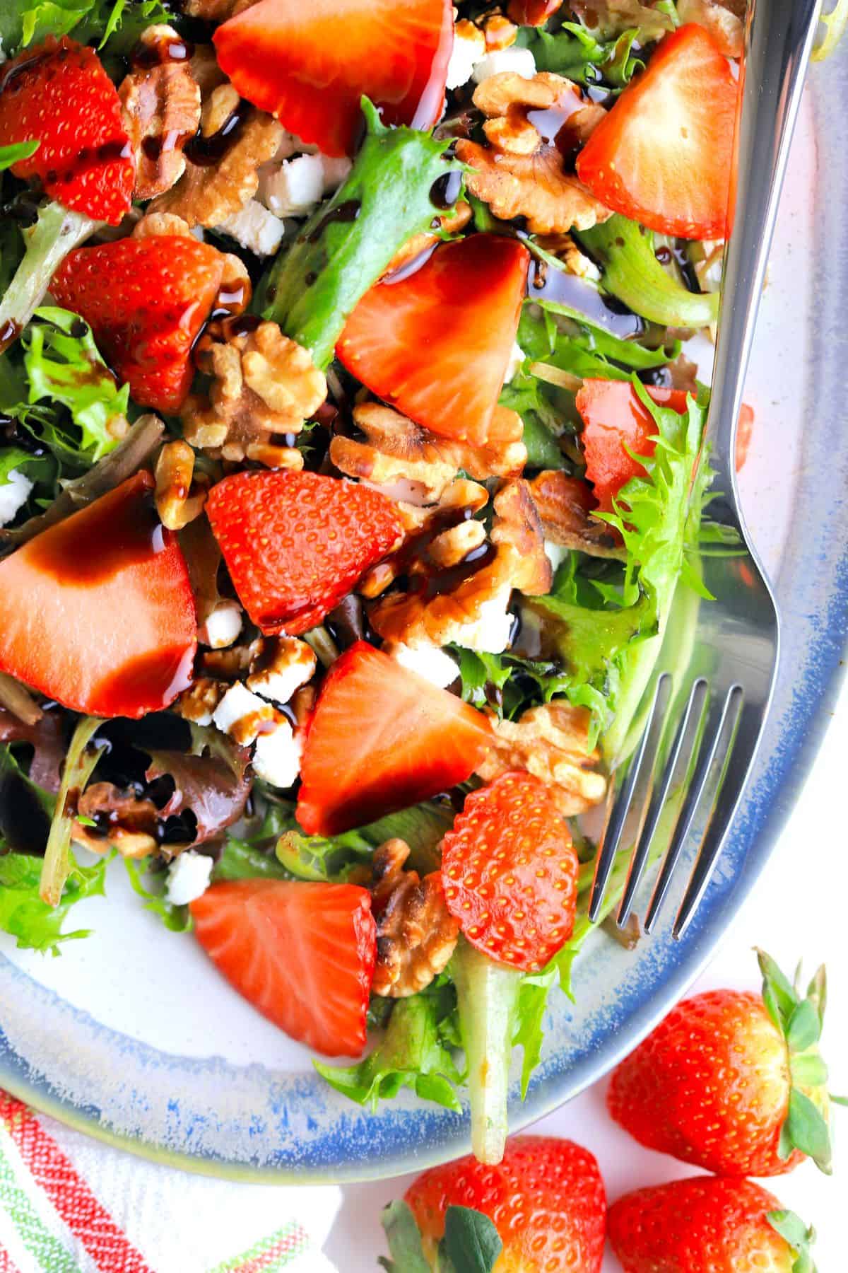 strawberry goat cheese salad on a blue rimmed platter with a fork.