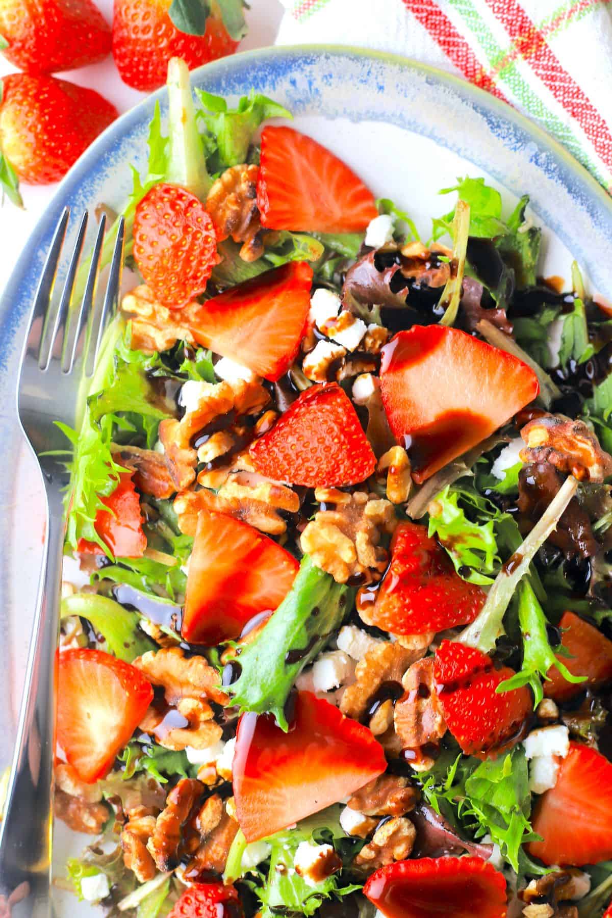 strawberry goat cheese salad on a blue rimmed platter with a fork.