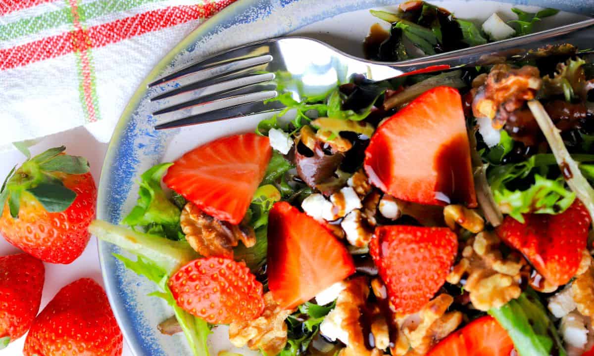 strawberry goat cheese salad on a blue rimmed platter with a fork.