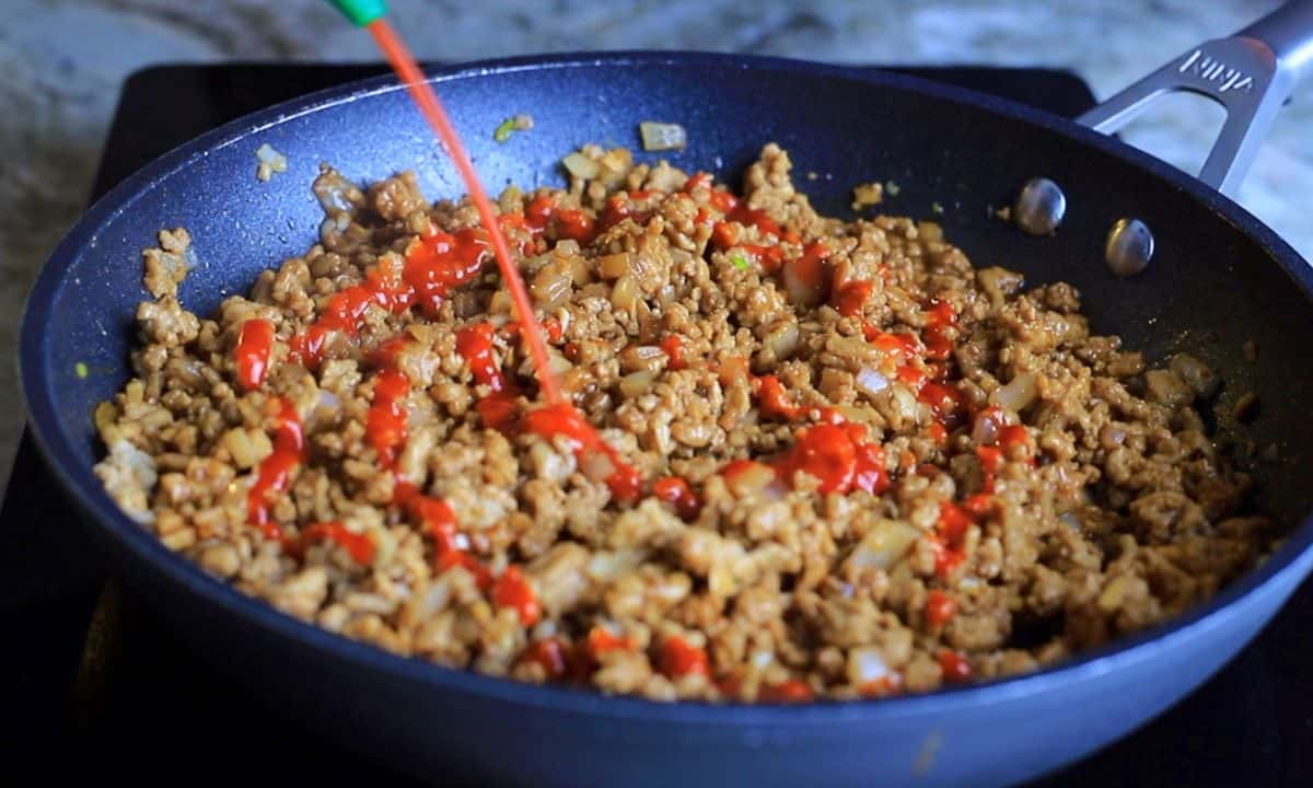 squirting sriracha onto the ground chicken in the frying pan.