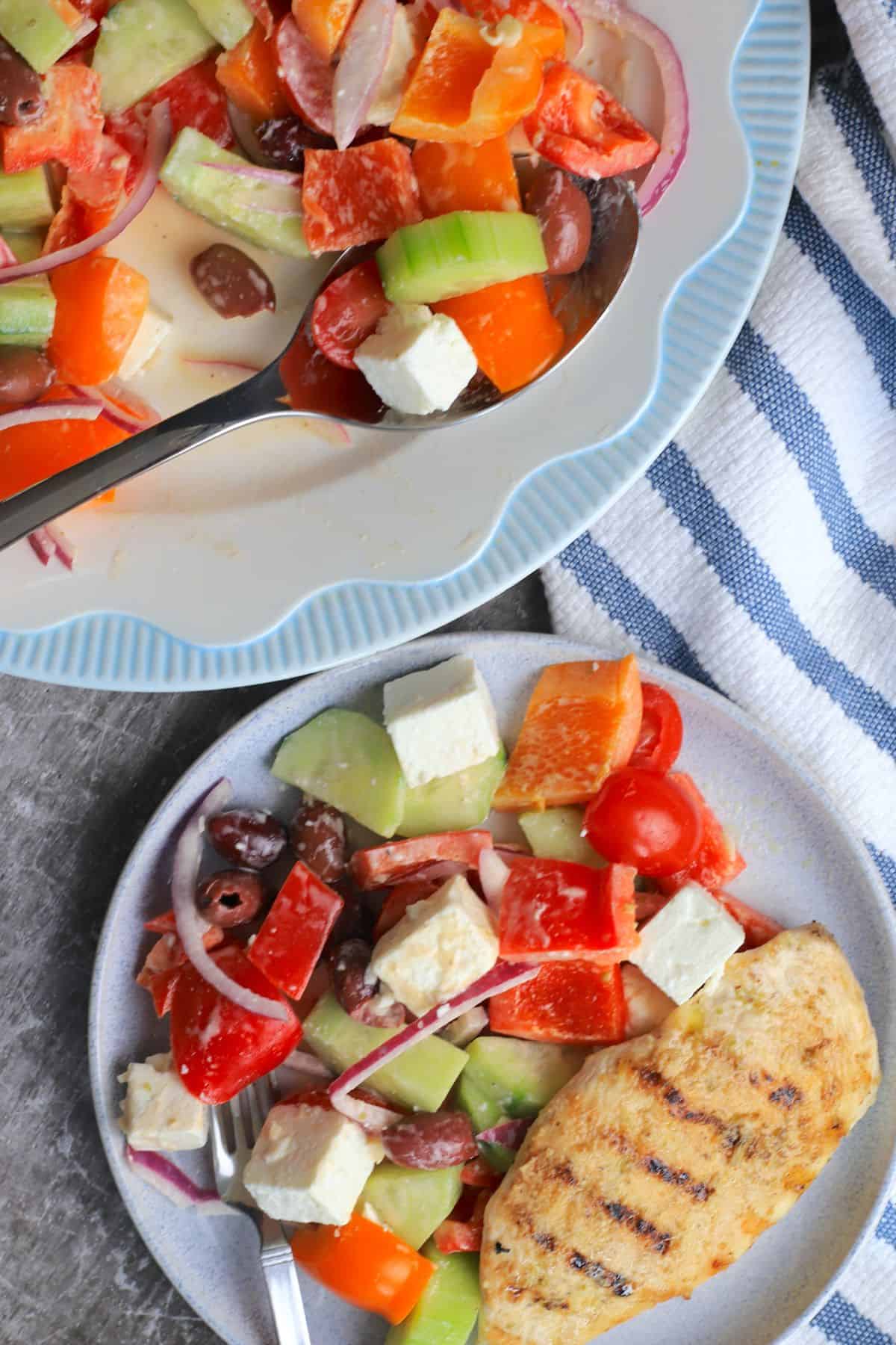 creamy keto greek salad on a blue rimmed white plate with grilled chicken.