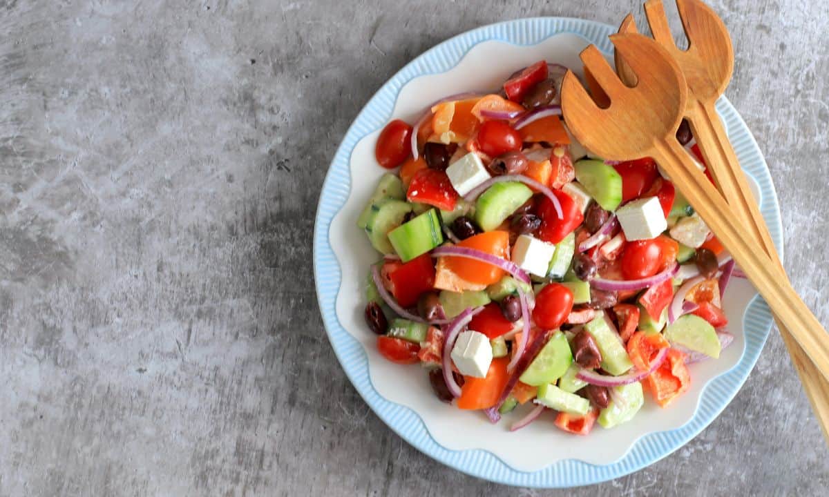 creamy keto greek salad on a blue rimmed white plate with woodend salad spoons.