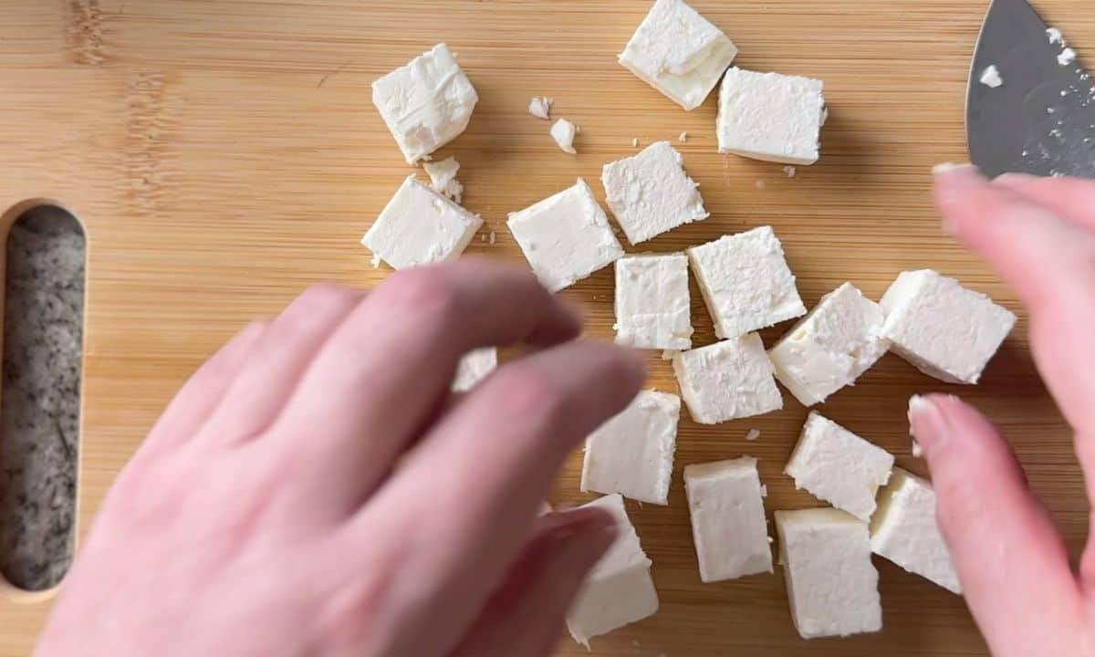 feta cheese cut into cubes on a wood cutting board.