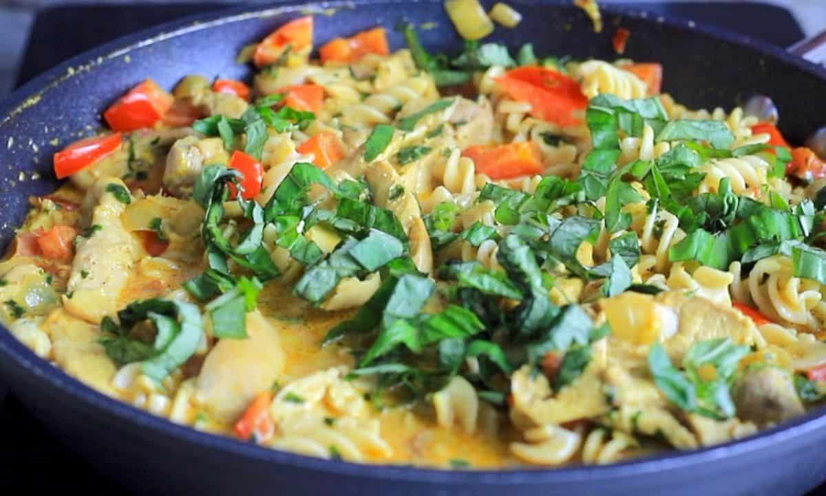 thai chicken curry pasta in a skillet topped with fresh basil.