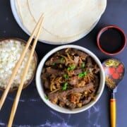 moo shu beef in a bowl next to a bowl with cauliflower rice and chopsticks with another dish with tortillas.