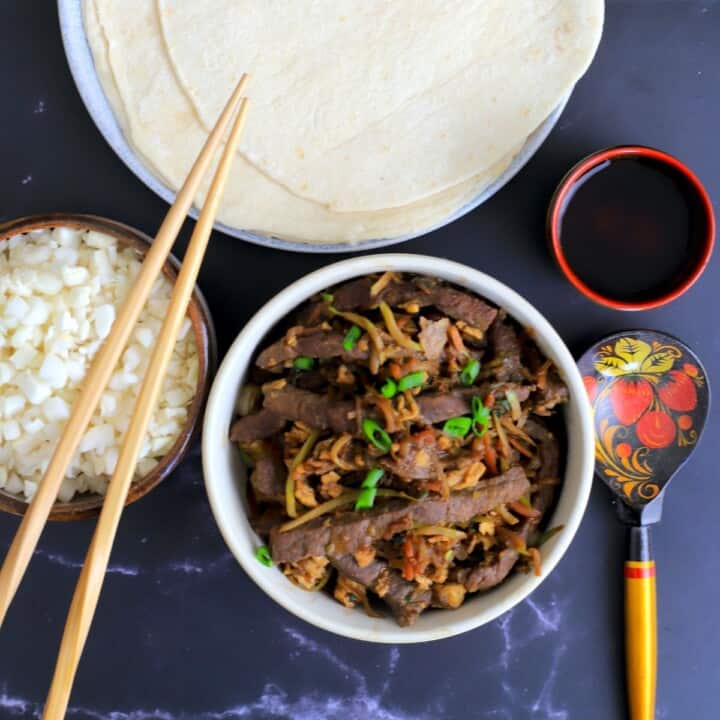 moo shu beef in a bowl next to a bowl with cauliflower rice and chopsticks with another dish with tortillas.