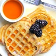 french toast waffles on on a plate with berries and a small bowl of maple syrup.
