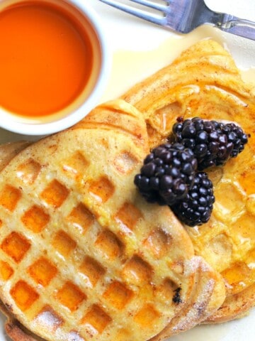 french toast waffles on on a plate with berries and a small bowl of maple syrup.