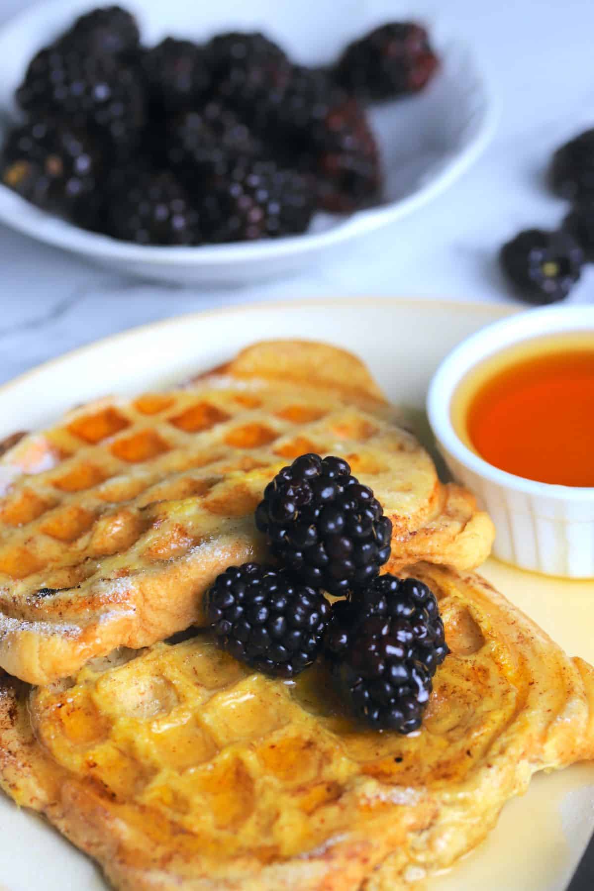 french toast waffles on on a plate with berries and a small bowl of maple syrup.