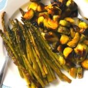 asparagus and brussels sprouts on a blue rimmed dish with serving spoons.