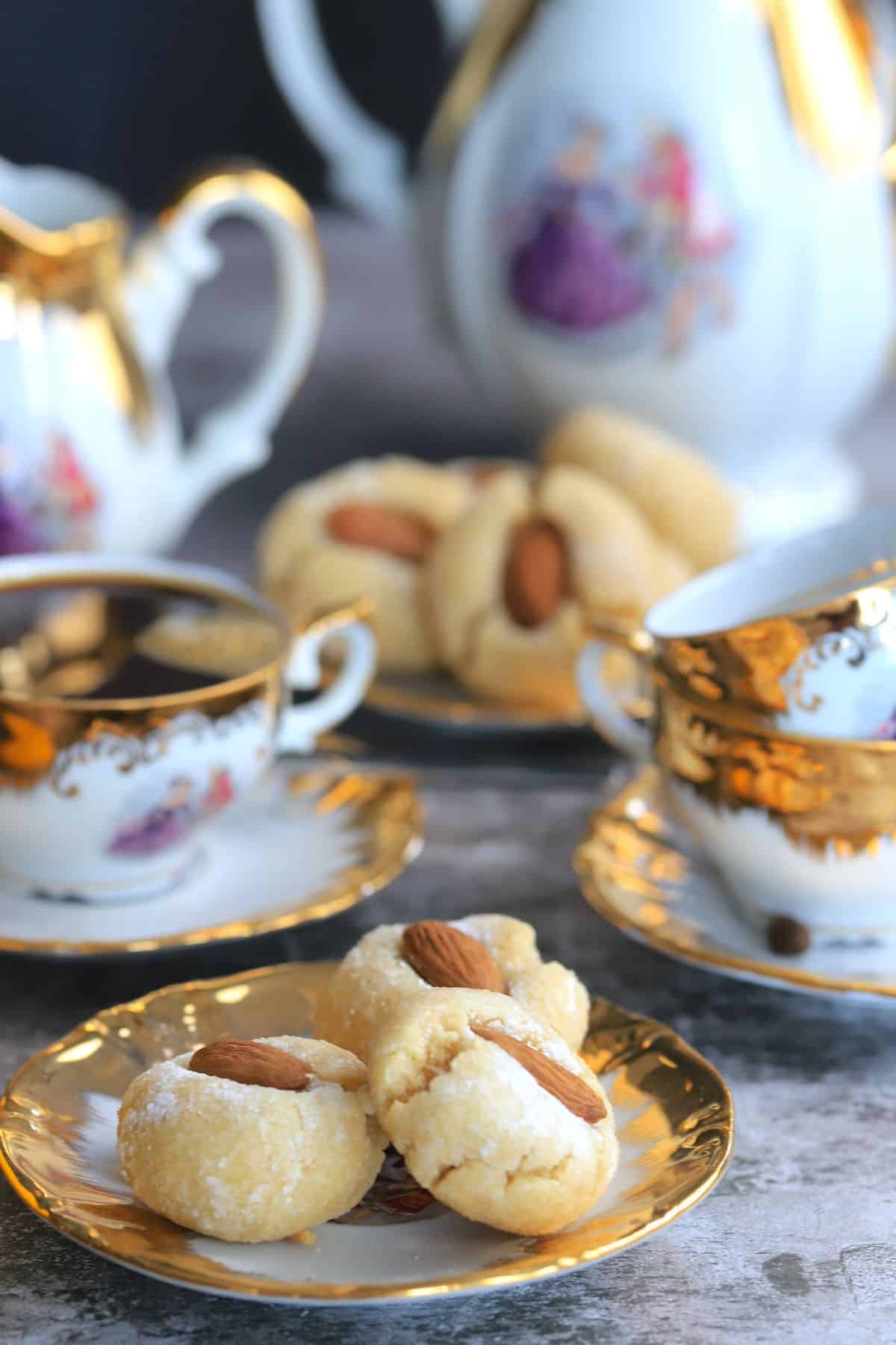 sicilian almond cookies on a gold rimmed dish surrouneded by gold rim tea cups and sets.