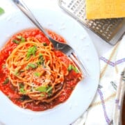 bowl with spaghetti arrabiata garnished with parmesan and basil leaves next to a cheese grater and parmesan.
