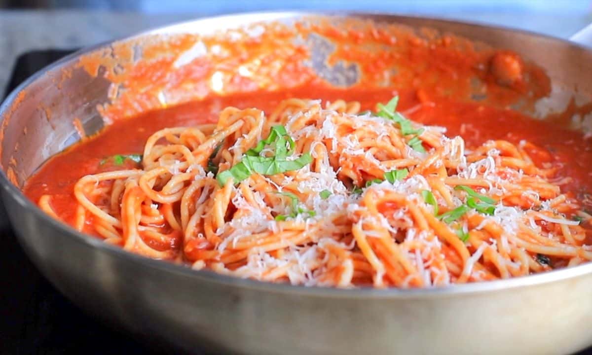 spaghetti arrabiata in a skillet garnished with grated parmesan and basil.