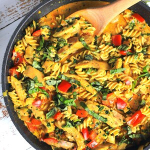 thai chicken curry pasta in a skillet with a wooden spoon.
