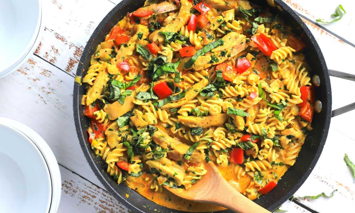 thai chicken curry pasta in a skillet with a wooden spoon.