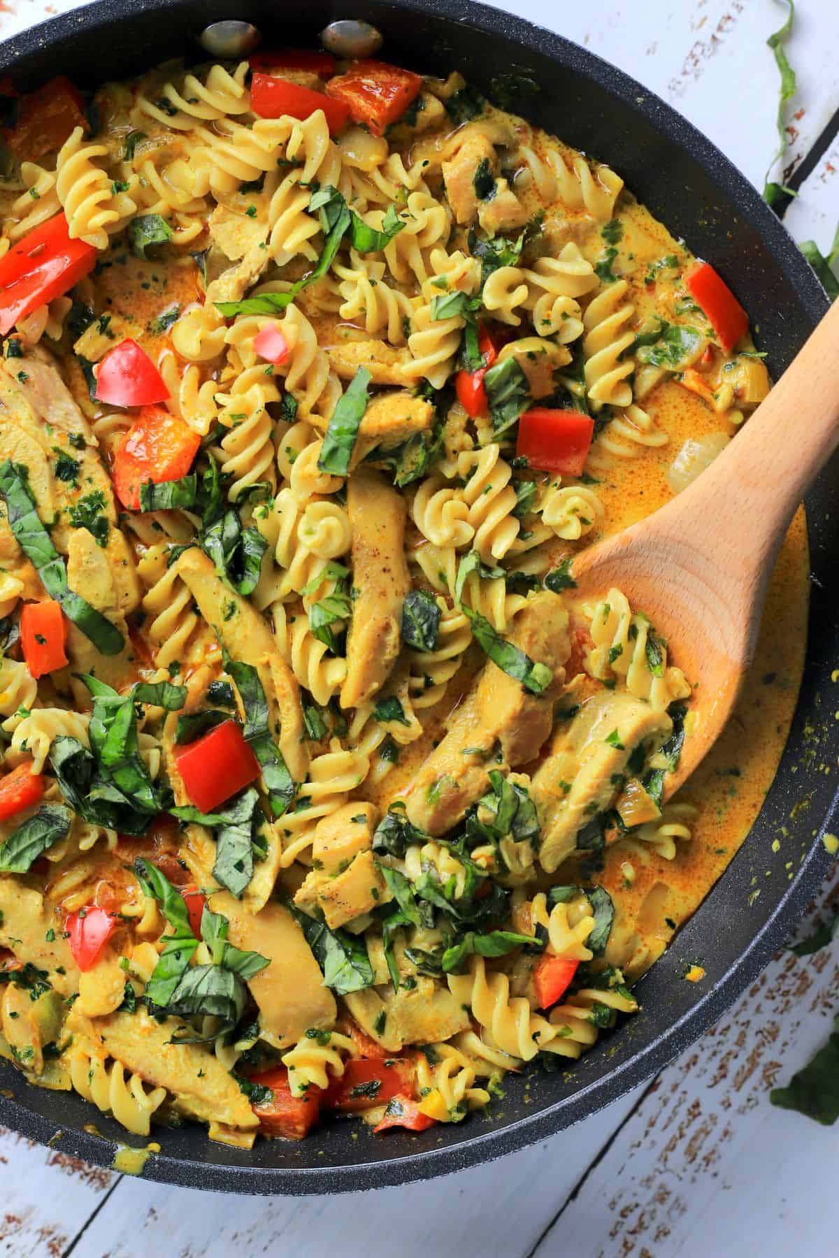 thai chicken curry pasta in a skillet with a wooden spoon.