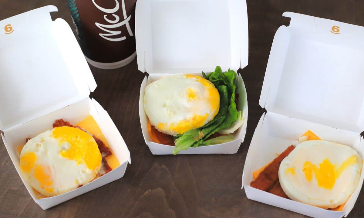 Three open takeout packages each with a round egg and bacon, one has lettuce.