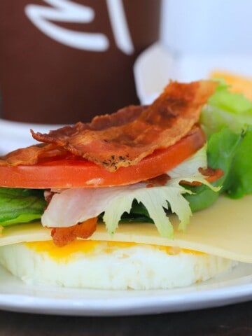 a white plate with a round egg, cheese, lettuce, tomatoe and bacon on top.