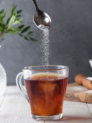 glass of tea while a spoon above sprinkling sweetener in it.