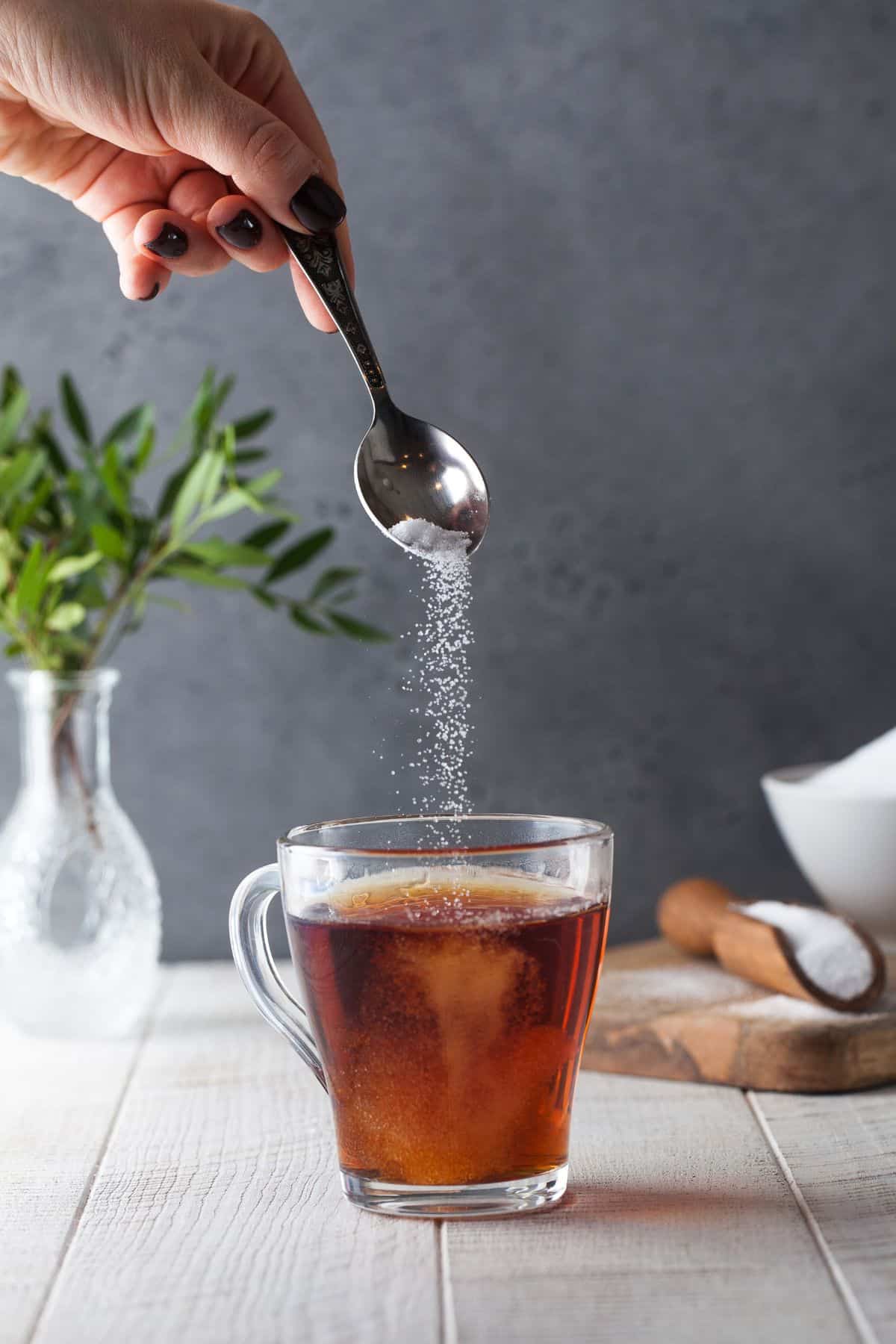 glass of tea while a spoon above sprinkling sweetener in it.