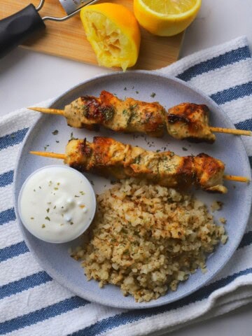 Low carb chicken souvlaki with tzatziki and lemon cauliflower rice on a plate next to a squeezed lemon.