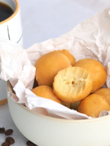 Maple protein coffee bites in a bowl lined with crumpled parchment paper next to a cup of coffee.