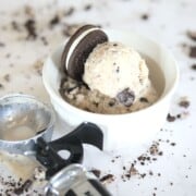 cookies and cream ice cream in a small white bowl next to an ice cream scoop.