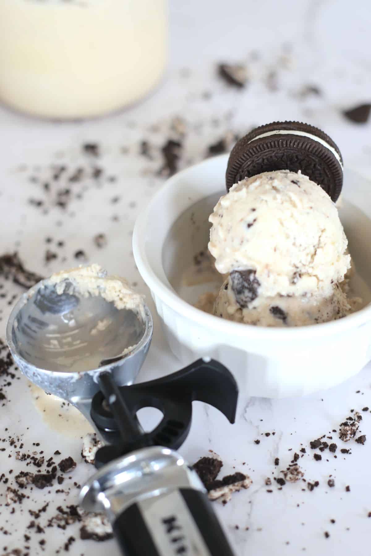 cookies and cream ice cream in a small white bowl next to an ice cream scoop.