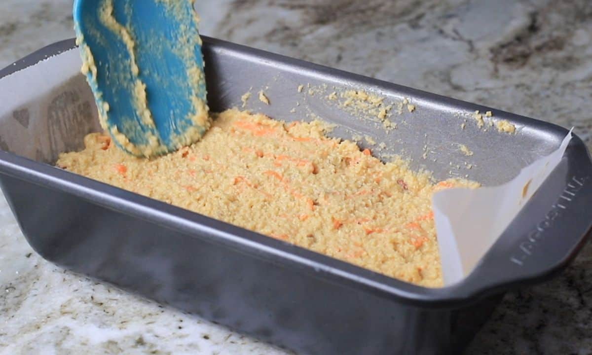 carrot cake batter in a loaf plan with a blue rubber spatula on top.