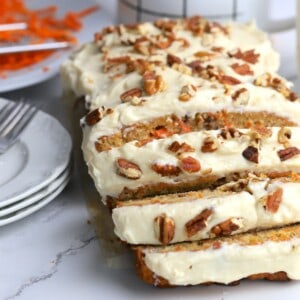 Sugar free carrot cake next to a coffee mug, dessert plates and shredded carrots.